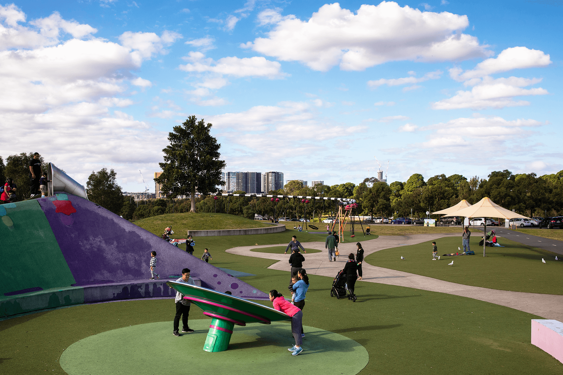 Many visitors at the Park doing various activities and using playground equipment.