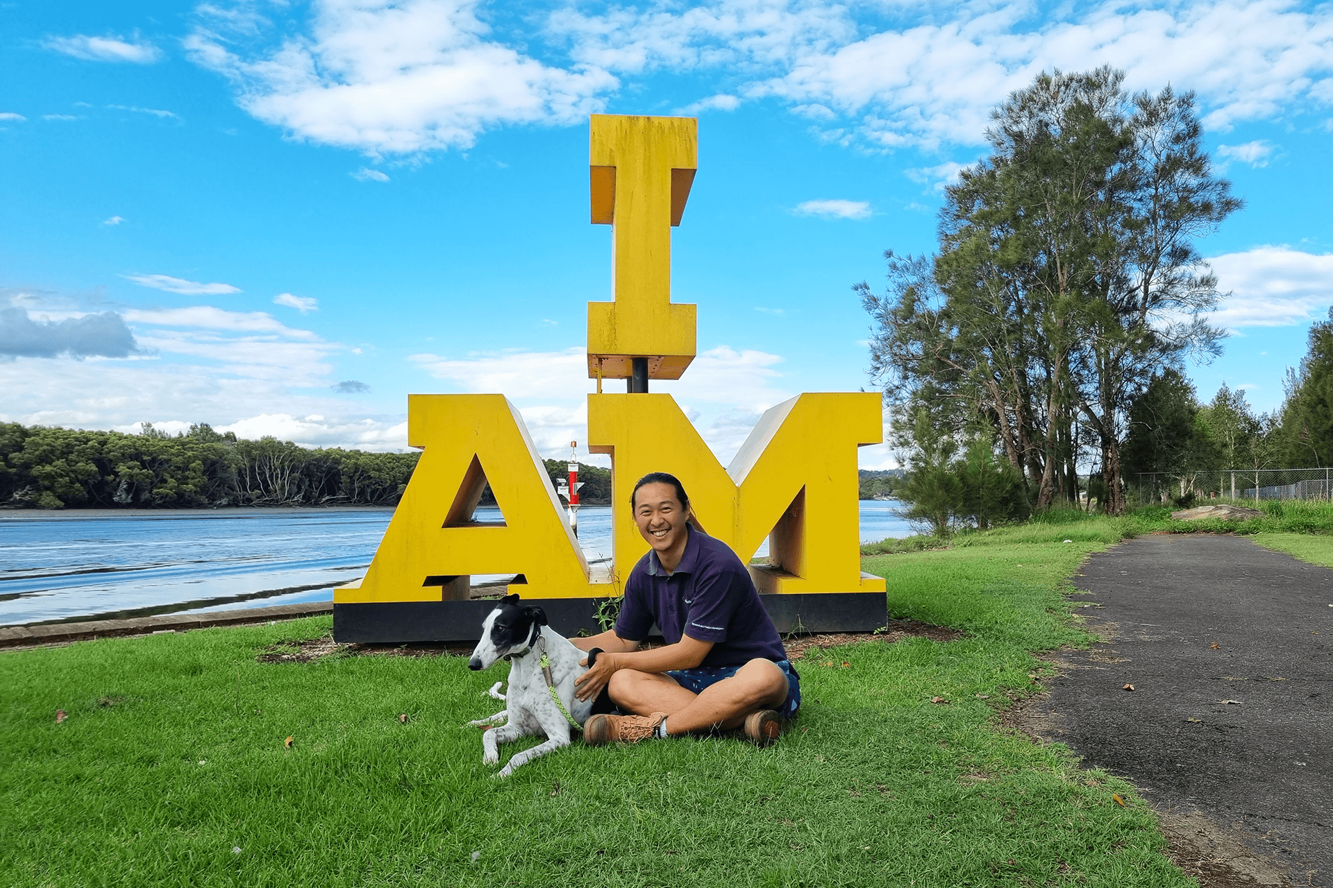 Person with dog in front of a sculpture in shape of letters "I" and "am" next to Parramatta River.