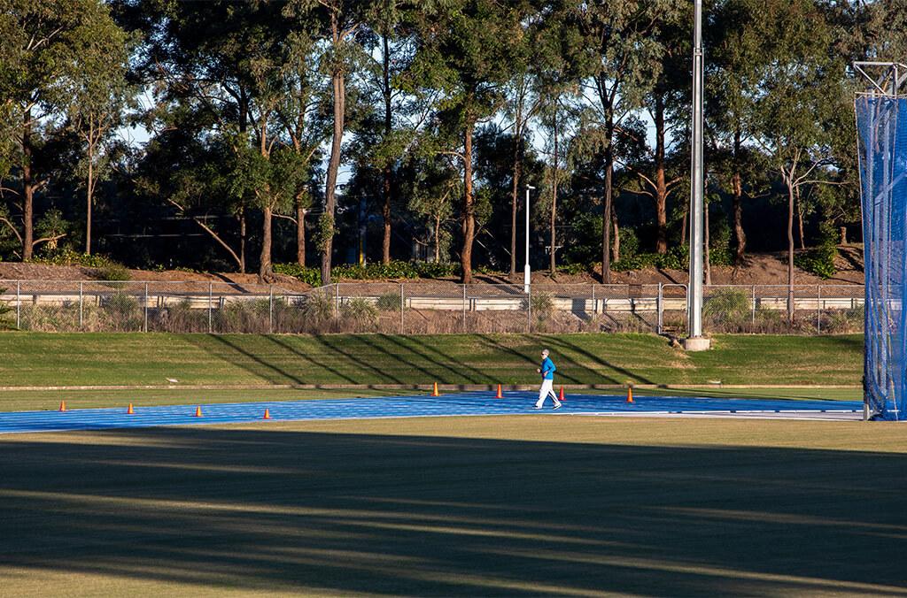 Man walking along athletic blue track field at the Athletic Centre