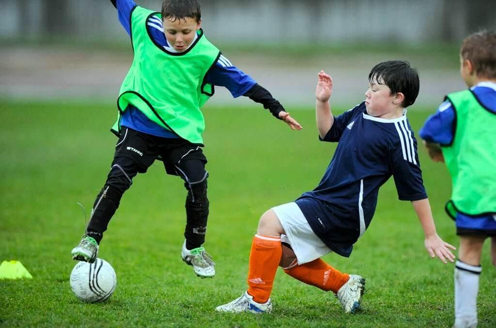 Kids kicking soccer ball around large grass field at the Tom Wills Community Field